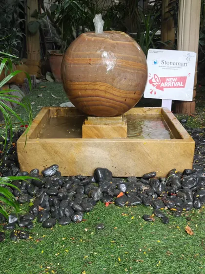 The complete setup of the Rainbow Sandstone sphere fountain, surrounded by decorative pebbles for a finished look.
