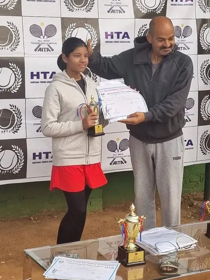 Mehr Muralidass receives her trophy for reaching her first AITA CS U-12 singles final in Gurgaon. The table is filled with trophies, highlighting the scale of the tournament.