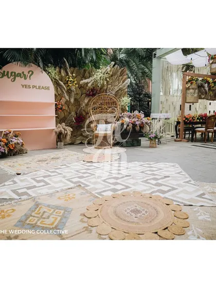 A mix of patterned and jute rugs defines the seating area, adding warmth and texture to the floor. In the center, a peacock chair provides a special seat for the bride, while a fun "Sugar? Yes Please" sign points to a cotton candy station.