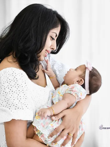 A mother gazes lovingly at her baby girl in this brightly lit, natural-style portrait. This image captures the simple, beautiful moments of early motherhood.