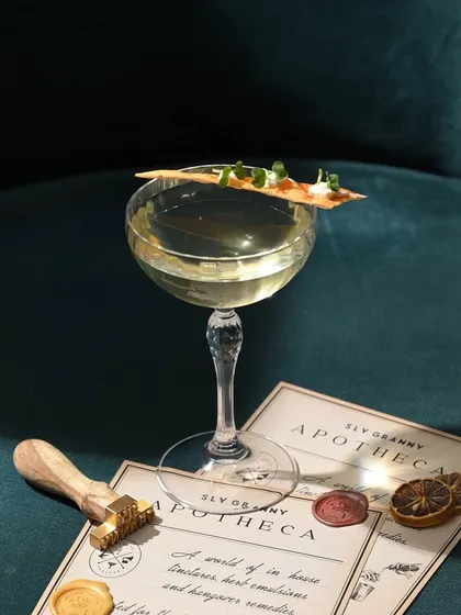 Magnificent Desolation, served elegantly in a coupe glass with a unique, savory crisp on top. It’s a drink for dreamers and adventurers.