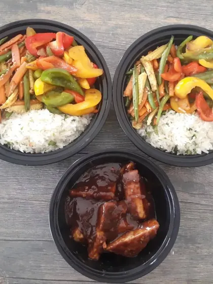 A complete meal delivery of rice bowls with stir-fried vegetables and a side of peanut butter tofu in a rich sauce.