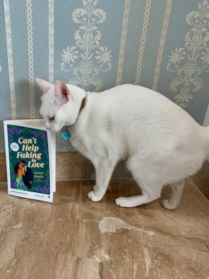 My cat giving my second novel, *Can't Help Faking in Love*, a curious sniff. She's my number one supporter (when she's not sleeping).