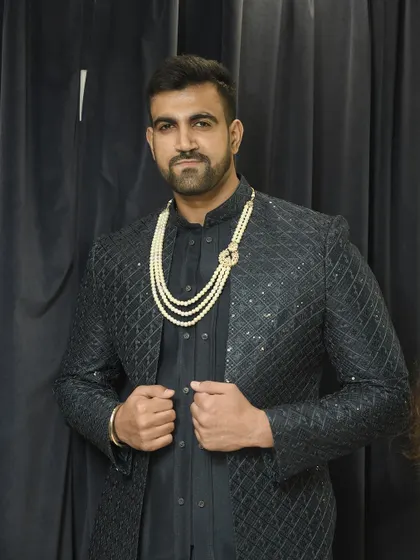 A confident pose from the client, showcasing the complete royal look with the pearl necklace against the dark Indo-western jacket.