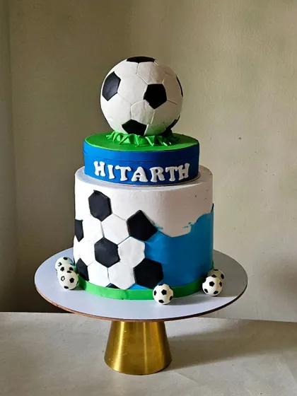 A dynamic football-themed cake with a rotating top tier. The bottom tier features a soccer ball pattern, while the top tier is a full, edible football that spins.