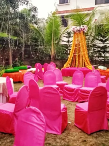An outdoor Haldi function setup with bright pink chair covers and a simple, elegant seating area decorated with marigold garlands.