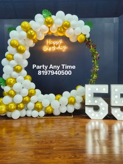 A simple and modern 55th birthday setup with a white and gold balloon arch and large marquee numbers.