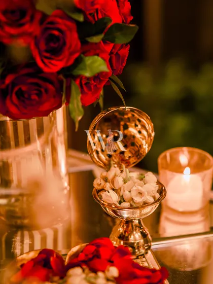 A small, ornate brass bowl filled with fragrant mogra buds sits beside a red rose arrangement. These traditional details add a layer of sensory richness and cultural depth to the decor.