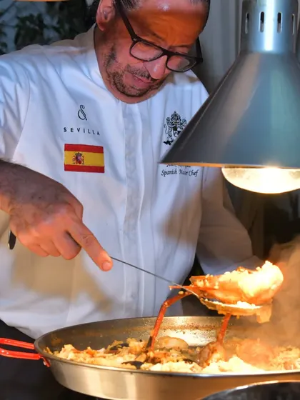 I am here preparing a large pan of paella over an open flame. This dish requires constant attention and care to ensure the rice cooks perfectly and absorbs all the flavour.