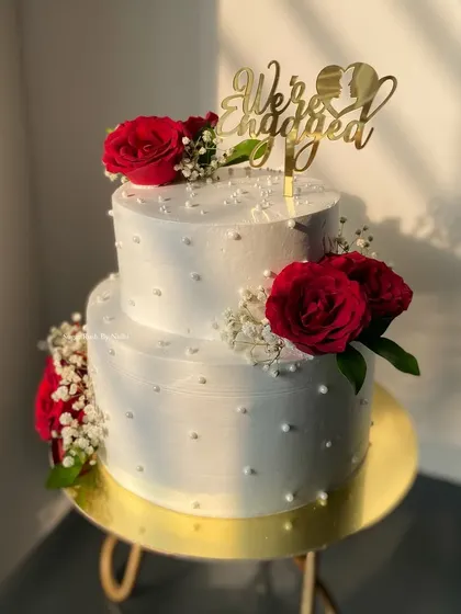 Simple, classic, and so romantic. This two-tier engagement cake features clean white frosting, pearl details, and is decorated with beautiful fresh red roses.