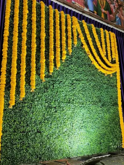 A simple backdrop with a green mat and marigold garlands, perfect for budget-friendly traditional events.