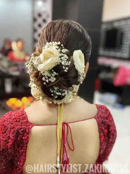 A close-up of a beautiful bridal bun adorned with fresh white roses and baby's breath. The texture in the bun adds a modern touch.