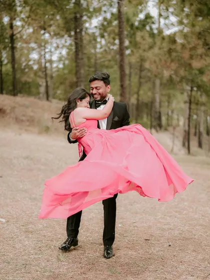 A romantic moment from a pre-wedding shoot in the hills of Himachal. The groom lifts his bride, her pink gown flowing, surrounded by the serene beauty of a pine forest.