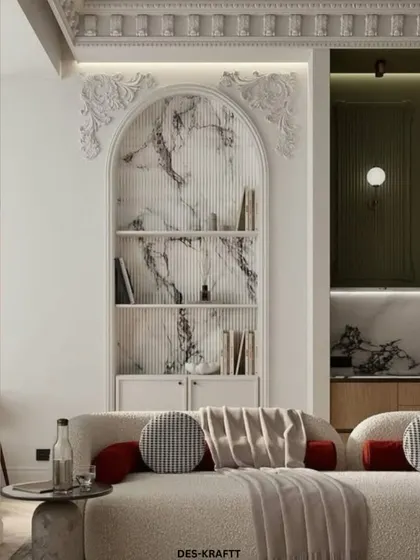 An arched marble-backed bookshelf serves as a stunning architectural feature in this living room, complemented by a textured bouclé sofa with bold rust-colored pillows.