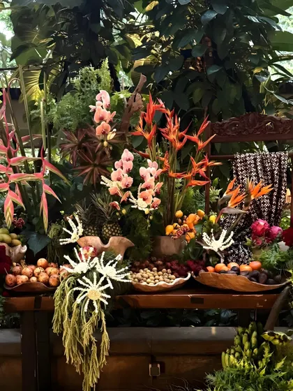 A lavish fruit and floral display on a rustic wooden cart. The arrangement includes exotic flowers like orchids and birds of paradise, alongside tropical fruits, creating a vibrant and abundant look.