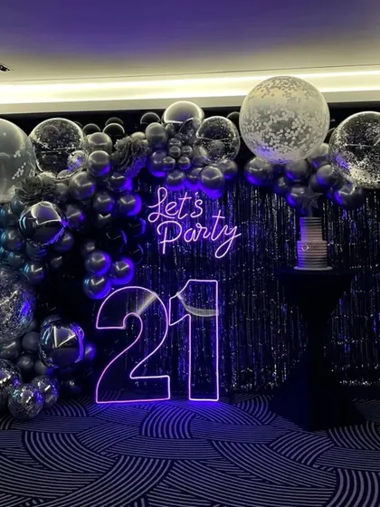 For this 21st birthday, we went for a chic and modern party vibe. The centerpiece is the glowing neon signage, including the age and a 'Let's Party' sign. I paired it with a dramatic backdrop of a silver tinsel curtain and a cascade of chrome and confetti balloons for a truly stylish celebration.