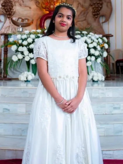 An angelic look for a milestone celebration. This full-length white gown features delicate lace sleeves and intricate embroidery on the bodice and skirt, making it a beautiful choice for a First Communion or other formal ceremony.