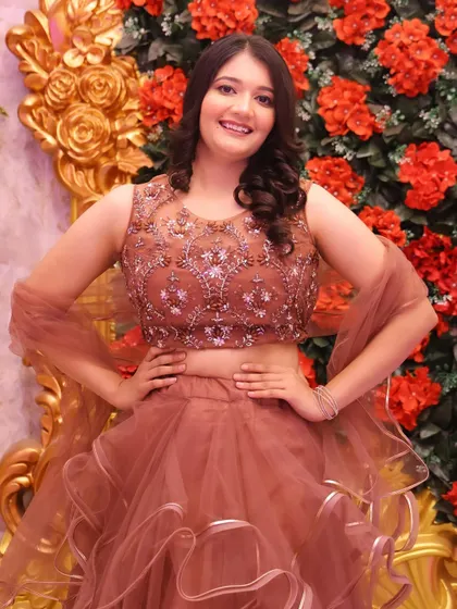 Posing against a floral backdrop, her makeup looks fresh and radiant. The soft curls complete this lovely party look.