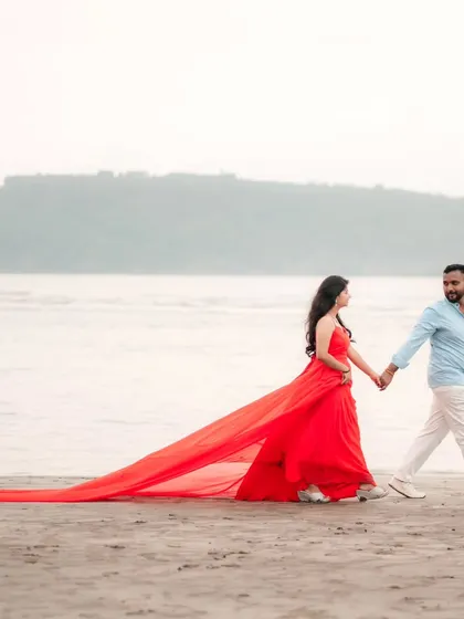Walking hand-in-hand into their future. The red trail gown follows them like a whisper on the sand, adding a touch of romance to their beach pre-wedding shoot.