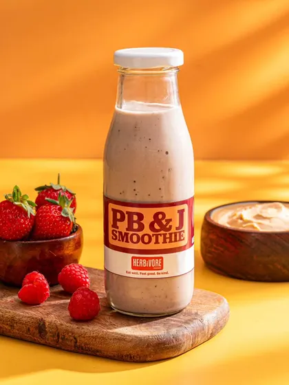 A PB&J smoothie from Herbivore Farms, styled with fresh berries against a bright orange background. This shot is clean, modern, and appetizing.