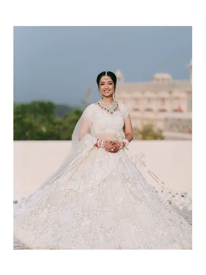 A grand, full-length shot of the bride, showcasing her magnificent white lehenga. The palatial background adds to the regal and majestic feel of this stunning portrait.