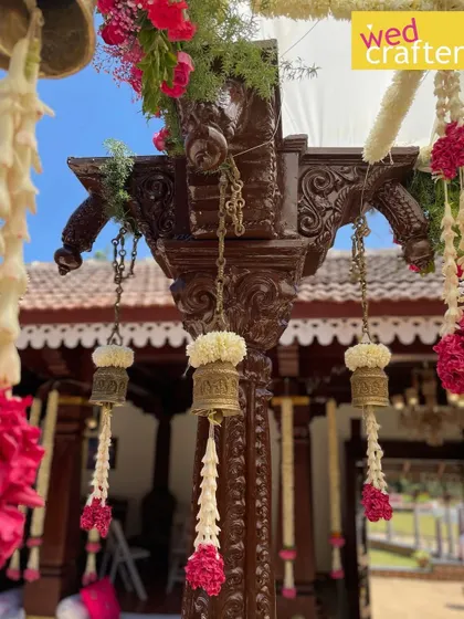 A detailed shot of a carved antique wooden pillar from the mandap, adorned with traditional flowers and brass bells, showcasing the craftsmanship.
