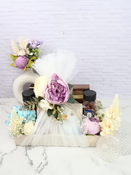 A luxurious wedding trousseau hamper featuring gourmet treats and floral arrangements. The items are elegantly wrapped in net and placed in a decorative tray, perfect for presenting as a wedding gift.