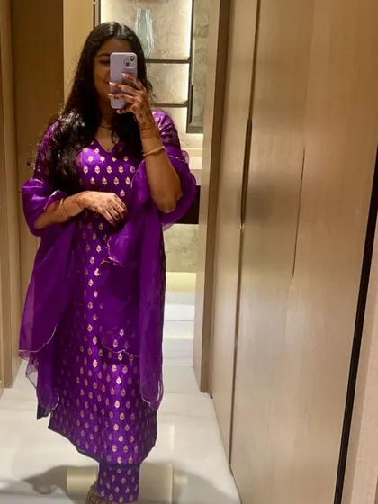 A client's mirror selfie showing off her vibrant purple brocade suit. The rich color and traditional pattern make it a standout piece for any festive occasion.