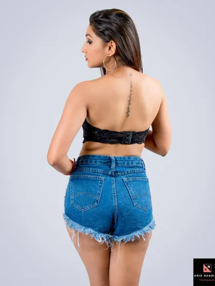 A chic and modern look featuring denim shorts and a black crop top. This back-facing shot highlights the model's spine tattoo and confident posture, perfect for a youthful fashion brand.
