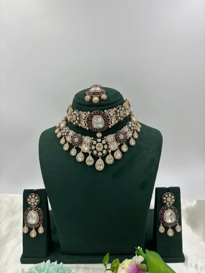 A double-layered bridal set combining a choker and a longer necklace. This design uses large Moissanite stones with deep red and green Meenakari, offering a complete and luxurious look for a bride.