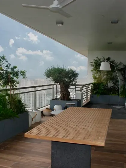 A balcony garden in Camellias, Gurugram. The space features a wooden deck, a dining table, and an olive tree in a planter, creating a perfect spot for an afternoon tea in winter.