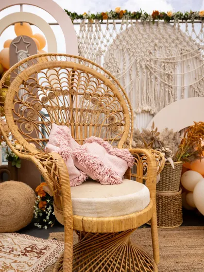 A beautiful peacock chair, a signature element of a boho-themed event. This chair, placed against a backdrop of macrame and balloons, serves as a perfect throne for the mom-to-be.