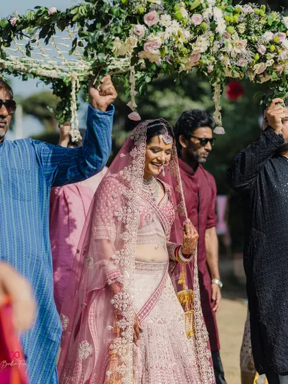 The bride's beautiful entrance under a floral phoolon ki chadar, a classic and emotional moment from a sun-drenched daytime wedding.