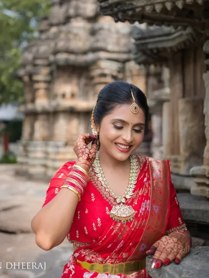 A bride in a vibrant red saree, posing against the backdrop of a historic temple. Her custom red blouse is adorned with delicate embroidery, perfect for a pre-wedding photoshoot.