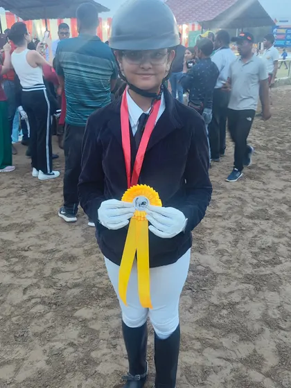 The smile of a champion. This young rider proudly displays her ribbon after a great performance, showing the joy that comes with equestrian sports.