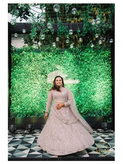 The bride twirling in her beautiful lavender lehenga in front of a lush green photo wall.