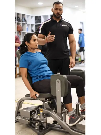 A trainer explains the mechanics of the hip adduction machine to a client, ensuring she understands the exercise before she begins.