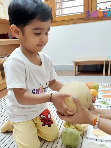 A boy holds a large melon, feeling its weight and texture. Direct sensory exploration with real objects is a cornerstone of Montessori learning.