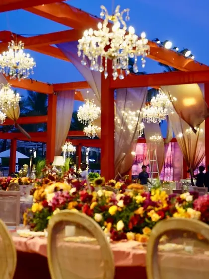 A sunset-soaked reception in Goa, with long tables adorned with lush, colorful florals and dozens of sparkling crystal chandeliers hanging overhead.
