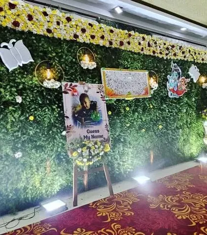 A naming ceremony backdrop with a green wall, floral moon accent, and a personalized welcome easel. The hanging cradle is decorated with flowers to match the theme.