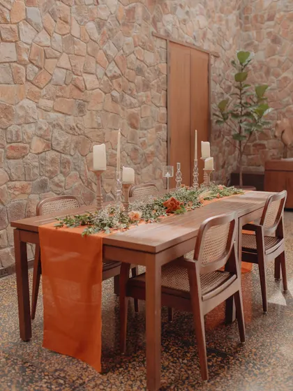 An indoor dining table is set with a vibrant orange runner and a simple green centerpiece. This shows how we can bring color and life to our indoor spaces as well.