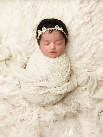 A beautifully simple portrait of a newborn swaddled in a cream-colored wrap on a soft, fluffy surface. Sometimes, simplicity is the most elegant way to capture a baby's beauty.