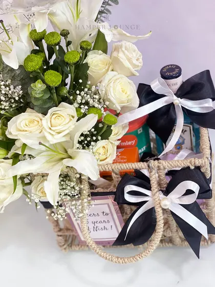 A close-up look at the details of my jute basket birthday hamper. You can see the fresh white lilies and roses, a personalized gift tag, and carefully wrapped presents with elegant black and white ribbons, showing the care that goes into every arrangement.