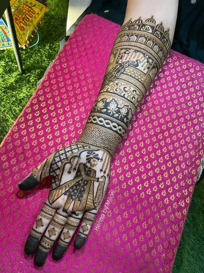 A full-arm bridal mehendi with a portrait of the groom. The design also includes peacocks and architectural elements, creating a regal and personal look.