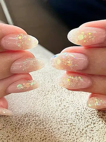 A close-up of sheer nails with embedded iridescent glitter, showing how they catch the light.