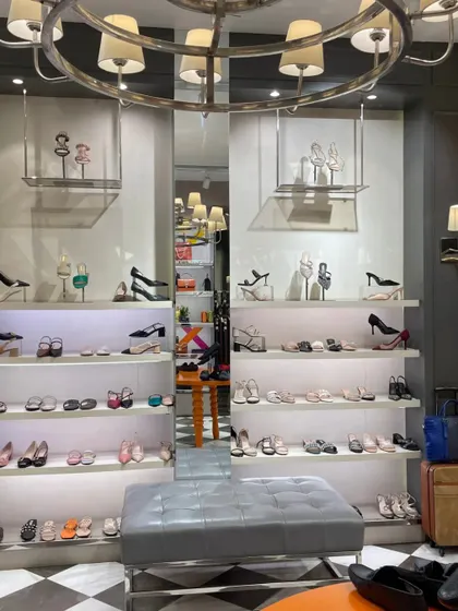 The shoe display section within the Rosso Brunello side of the store, featuring backlit shelves and a large, ornate chandelier.