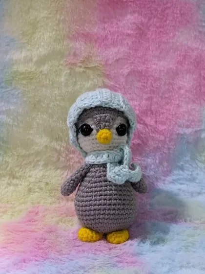 A tiny penguin wearing a light blue hat, standing against a colorful pastel background.