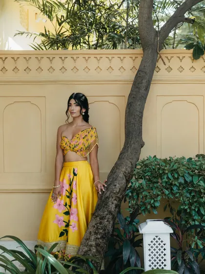 A serene bridal portrait against a yellow wall in Rajasthan. The bride's pose is relaxed and natural, capturing a moment of calm during the Mehendi celebrations.