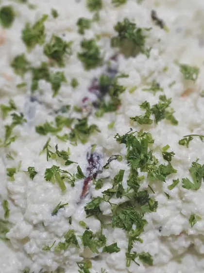 A bowl of cooling curd rice, garnished with fresh coriander, a perfect dish to balance the spicy flavors of an Indian meal.