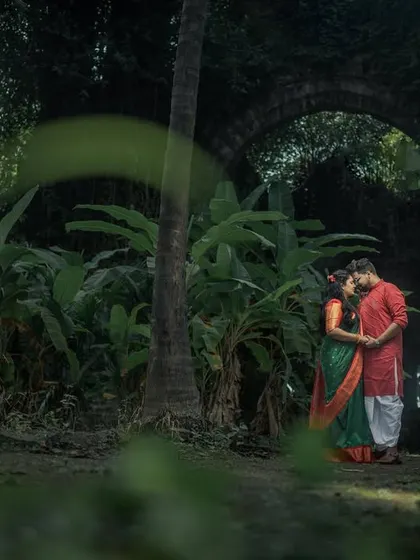 An intimate moment in a lush, green setting near a fort. The contrast between the traditional attire and the wild nature creates a beautiful, romantic scene.